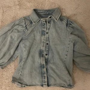 Ljusblå jeansskjorta med puffärm - Säljer en ljusblå jeansskjorta från Zara med puffiga trekvartsärmar och klassisk krage. Skjortan har knappar framtill och är gjord i bomull. Perfekt för dig som vill ha en chill men ändå trendig look. Storlek M men passar mig perfekt som har S!  Använt endast en gång