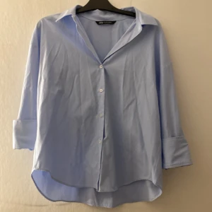 Ljusblå skjorta från Zara - Snygg ljusblå skjorta från Zara med klassisk krage och knappar framtill. rundad nederkant.  Perfekt för en clean och stilren look.