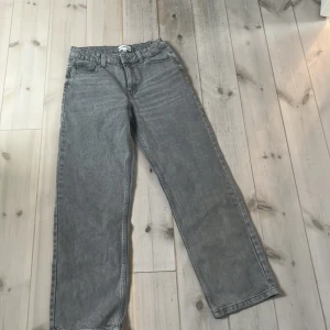 Grå jeansbyxor från D.M.D, storlek 158 - Snygga grå jeansbyxor från D.M.D By denim day i rak modell med klassiska fem fickor och bälteshällor. Jeansen har en normal passform och är tillverkade i slitstarkt denimtyg. Perfekt för dig som gillar en enkel och clean look.