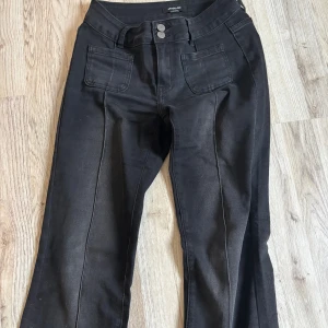 Svarta bootcut jeans från Madlady - Säljer ett par svarta jeans från Madlady med bootcut passform och hög midja. Byxorna har framfickor med markerade sömmar, dubbla knappar i midjan och bakfickor med knappdetalj. Materialet är jeans och modellen är lite kortare.