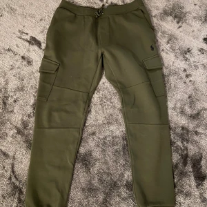 Olivgröna cargopants från Polo Ralph Lauren - Snygga olivgröna cargopants från Polo Ralph Lauren med dragsko i midjan och stora fickor på sidorna. Byxorna har en avslappnad passform och är tillverkade i mjukt bomullsmaterial. Perfekta för en chill och trendig look.