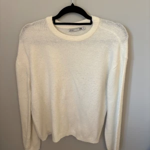 Vit stickad tröja från 157 - Mysig vit stickad tröja från 157 med rund halsringning och långa ärmar. Enkel och stilren design som passar perfekt till lager-på-lager under kyliga dagar. Ribbstickade muddar vid hals, ärmslut och nederkant.