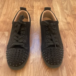 Christian Louboutin svarta sneakers med nitar - Svarta sneakers från Christian Louboutin i mocka med coola svarta nitar på tån och klassisk röd sula. Sparsamt använd och fortfarna i super skick behöver vara tvättas. Säljer på grund av att jag har ändrat still och har inte behov av de längre