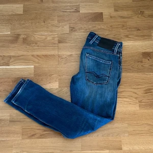 Replay Anbass slim fit jeans blå - Snygga blå Replay Anbass jeans i slim fit med klassisk femficksdesign och diskreta slitningar. Jeansen har normal midja och raka ben med snygg tvätt och kontrastsömmar. Perfekta för dig som gillar en stilren och modern look.