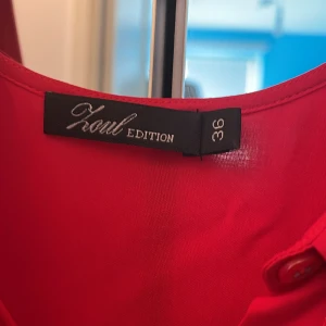 Röd ärmlös skjor Karl Edition - Snygg röd skjorta  från Karl Edition i storlek 36. Klänningen är ärmlös med klassisk krage och knappar framtill. Materialet är mjukt och har ett lätt fall, perfekt för dig som gillar en enkel men stilren look.