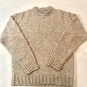 Beige stickad tröja från Jack & Jones - Beige stickad tröja från Jack & Jones med rund hals och ribbade muddar. Enkel och stilren design som passar perfekt till lager-på-lager. Mjuk och skön känsla, perfekt för kyligare dagar. Fraktar inom 24 timmar och pris kan diskuteras. Skriv gärna om frågor eller intresse