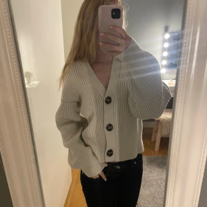 Beige ribbad kofta med stora knappar - Säljer en beige ribbstickad kofta med oversized passform och stora, mönstrade knappar framtill. Koftan har v-ringning och långa ärmar med breda muddar. Perfekt att slänga på sig för en chill och snygg look.