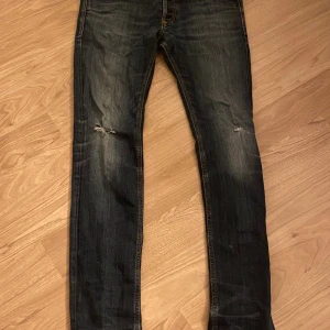 Diesel jeans mörkblå med små slitningar  - Snygga mörkblå jeans från Diesel med slitningar på knäna och klassiska fem fickor. Jeansen har en smal passform och är tillverkade i robust denim med snygga detaljer och kontrastsömmar. Perfekta för dig som gillar en cool och avslappnad stil.