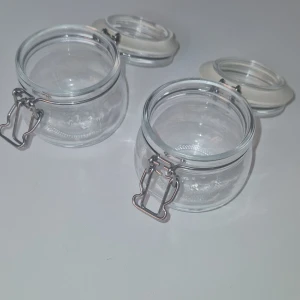 Glasburkar - Bilderna visar två små glasburkar med tätslutande lock och metallspänne. Perfekta för förvaring av kryddor, småsaker eller dekoration. Burkarna är i mycket gott skick utan synligt slitage eller defekter. Klara och rena, redo att användas direkt. Glasburken kan diskas i diskmaskin, men gummipackningen bör handdiskas. 