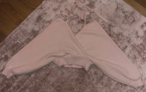 Ljusrosa ribbad topp med knytband - Trendig ljusrosa ribbad topp med långa ärmar och knytband på axlarna (axelband). Toppen har en croppad passform och är tillverkad i ett mjukt stickat material. Tröjan är en kortare modell. Perfekt för att skapa en söt och avslappnad look.