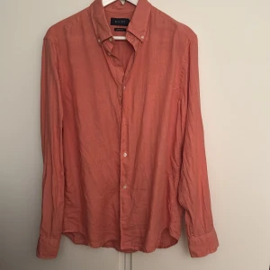 Korallfärgad linneskjorta från Riley - Snygg korallfärgad skjorta från Riley i regular fit. Skjortan är tillverkad i linne, har klassisk krage, knäppning framtill och långa ärmar. Perfekt för dig som vill ha en luftig och stilren look. Använt den 1 gång 