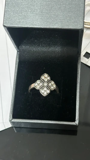 Silverring med glittrande stenar - Snygg silverfärgad ring med ett unikt korsformat mönster av glittrande vita stenar. Ringen har detaljerade kanter runt stenarna som ger extra bling och en lyxig känsla. Perfekt för dig som gillar att sticka ut med dina accessoarer.