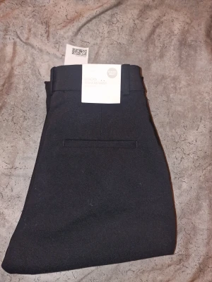 Svarta kostymbyxor med regular waist - Svarta kostymbyxor som är perfekta för en clean och stilren look. Materialet är mjukt och följsamt, vilket gör dem bekväma hela dagen.