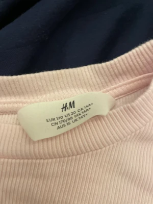 Rosa ribbad långärmad tröja H&M - Söt ljusrosa ribbad långärmad tröja från H&M med broderad nalle och trycket '1982 Athletic sport club' på bröstet. Tröjan har rund hals och är i mjuk bomull, perfekt för dig som gillar gulliga detaljer och chill stil.