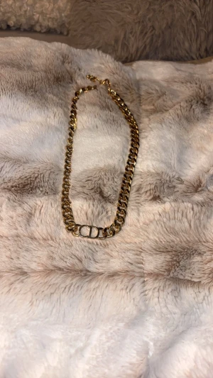 Guldigt kedjehalsband från Dior - Snyggt guldigt halsband från Dior med chunky kedja och klassisk CD-logga i mitten. Halsbandet har en rund bricka med Dior-gravyr vid låset och är tillverkat i metall med glansig finish. Perfekt statement piece för dig som gillar lyxiga accessoarer.