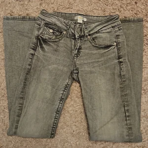 Ljusgrå lågmidjade bootcut jeans från Gina Tricot - Jag säljer ett par ljusgrå jeans från Gina Tricot i storlek 152. Modellen har låg midja, bootcut-ben, klassiska fem fickor och snygga detaljer på bakfickorna. Jeansen är använda ett fåtal gånger och har därför inga skador förutom ett litet hål som tyvärr blev i en av bakfickorna vid tidig användning, men som jag har sytt ihop själv så att det nu ser ut som en fin detalj istället, och en svag och knappt synlig fläck på ena känt. (Se bilder) Nypris runt 400 kr. 