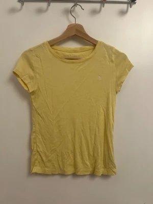 Gul t-shirt från Ralph Lauren - Säljer snygg gul t-shirt från Ralph Lauren med broderad logga på bröstet. Modellen är kortärmad och har en rund halsringning.