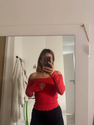 Röd offshoulder ribbad topp - Säljer en snygg röd offshoulder topp med ribbad struktur. Toppen är tight och har långa ärmar som sitter skönt över axlarna. Perfekt för dig som gillar att sticka ut med färg och vill ha en trendig look.