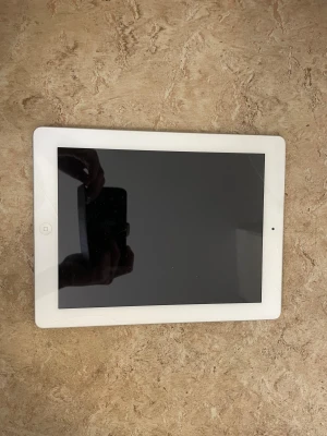Apple iPad 2 16GB - Apple iPad 2 med 16GB lagring, vit front och silver baksida. Skärmen har synliga sprickor och baksidan visar tecken på slitage. Perfekt för enklare surf och appar. Säljs i befintligt skick, idealisk som reservdelsplatta eller för den som vill ha en billig iPad.