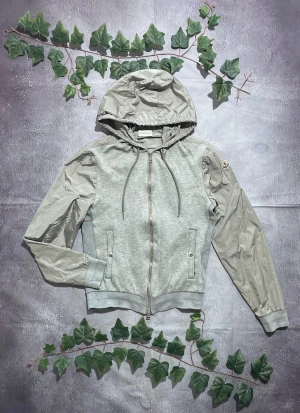 Moncler Maglia Cardigan i Grå och Beige Storlek S [ÄKTA] - 🎨 Färg: Grå och Beige 📏 Storlek: S ♻️ Skick: 8/10 – lättare bruksspår men inga större defekter 🧵 Material: Mjuk sweatshirt-tyg framtill och i kroppen, med nylonärmar och huva ✨ Detaljer: • Hybridmodell med mjukt tyg och lätt, vindresistent nylon • Avtagbar eller fast huva (huvan är nylon) • Dragkedja fram • Två framfickor med knappdetalj • Moncler-patch på vänster ärm • Ribbstickad nederkant och muddar • Perfekt som lätt jacka eller vardagsplagg ‼️ Skickas dagen efter köpet genomförs! ‼️