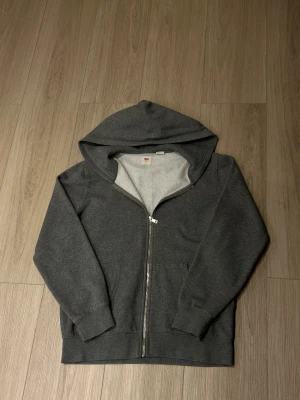 Grå hoodie från Levi's med dragkedja - Snygg mörkgrå hoodie från Levi's i storlek M. Tröjan har huva, hel dragkedja och två fickor framtill. Mjuk insida i fleece och klassisk Levi's-logga broderad på bröstet. Perfekt för chill dagar mer bilder eller frågor är det bara att ge mig en signal svarar oftast inom 1-2 timmar och skickas samma dag om man beställer innan 19:00