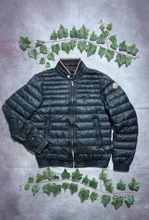 Moncler Garin Puffer Jacka storlek 3 (S/M) [ÄKTA] - 🎨 Färg: Mörkblå / Navy med Röd och VIta detaljer 📏 Storlek: Moncler Storlek 3, motsvara S/M ♻️ Skick: 10/10 inga synliga fläckar, hål eller defekter 🧵 Material: Lättviktsdun / quiltat yttertyg (ser ut som typisk dun- eller syntetfylld lättviktsjacka)   ✨ Detaljer:         •        Klassisk quiltad design         •        Hög krage med dekorativ knäppning och röd/vit kantband         •        Två framfickor med dragkedja         •        Ribbstickade muddar vid ärmslut och nederkant