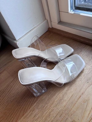 Klackar  - Säljer ett par trendiga klacka från Bershka i beige med transparenta remmar och chunky klack i klar plast. Snygg fyrkantig tå och öppen design som ger en modern vibe. Perfekta för dig som gillar statement-skor med coola detaljer.