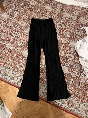 Svarta vida byxor med plisserat tyg - Säljer ett par svarta byxor med plisserat tyg och breda ben. De har en elastisk midja och är riktigt sköna att ha på sig. Passar dig som gillar en loose och trendig look med lite extra flow i steget.