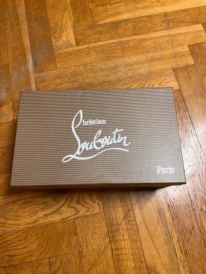 Helt nya Christian Louboutin - Snygga svarta sneakers från Christian Louboutin i mjuk mocka med klassisk röd sula. Skorna har rund tå, platt sula och snörning framtill. Perfekt för dig som vill ha en lyxig och stilren look med en ikonisk touch från Paris.
