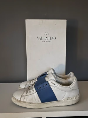 Valentino Garavani Open sneakers vit/blå - Snygga Valentino Garavani Open sneakers i vitt skinn med bred blå läderdetalj över sidan. Storlek 41. Hör av dig om du har några funderingar 