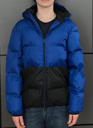 Blå och svart pufferjacka från Replay - Snygg blå och svart pufferjacka från Replay med stor logga på ryggen och patch på ärmen. Jackan har huva, dragkedja och är vadderad för extra värme. Perfekt för kalla dagar och ger en cool grish look. Inga slitningarnädtan aldrig använd. Säljer för att den är för liten för mig. Passar 167-175 . Nypris är 1800