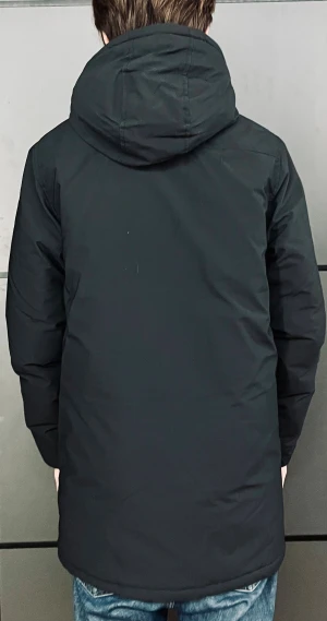 Svart parkas från Lyle & Scott - Svart parkas med huva från Lyle & Scott, prydd med deras klassiska guldfågel på bröstet. Jackan har två stora fickor framtill, två bröstfickor med dragkedja och en hög krage. Materialet är slitstark polyester och passformen är normal. Perfekt för kalla dagar.