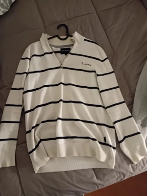 Vit randig tröja från Bondelid - Snygg vit långärmad tröja från Bondelid med svarta horisontella ränder och half zip framtill. Tröjan har ribbade muddar och krage, samt diskret Bondelid-logga på bröstet. Perfekt för dig som gillar klassisk och stilren design.         9/10 skick.