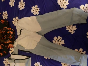 Nike ljusblå mjukisbyxor med snörning - Snygga mjukisbyxor från Nike i ljusblå och grå färgblock. Byxorna har elastisk midja med svart snörning och ribbade muddar vid benslut. Perfekta för chill eller träning, med klassisk Nike-logga på höften. Storleken är L men passar M fortfarande 