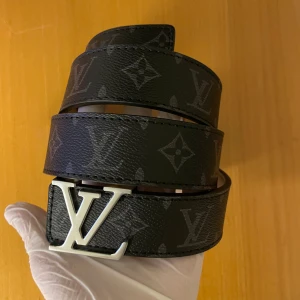 svart skärp med monogram - Säljer ett svart bälte med klassiskt monogrammönster och ett -spänne i silver. Bältet är gjort av skinn och har en lyxig vibe som verkligen sticker ut. Kommer med originalask och kvitto. Perfekt för dig som vill ha något extra till outfiten.