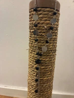 Silverfärgat halsband med svarta pärlor - Unikt halsband med silverfärgade runda plattor och svarta, facetterade pärlor. Kedjan är tunn och har flera dekorativa detaljer som ger ett coolt och stilrent intryck. Perfekt för dig som gillar att sticka ut med accessoarer som har både glans och kontrast.