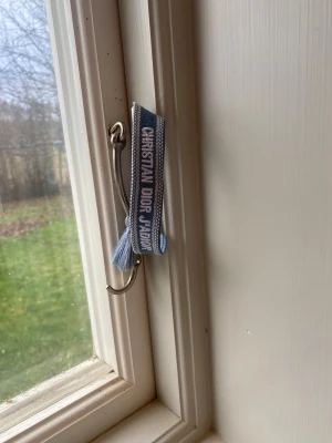 Blå Christian Di0rJ'Adi0r armband - Snyggt blått armband från Christia.n Di0r med texten 'J'Adior' broderad i vitt. Armbandet har en justerbar knytning och dekorativa tofsar i ändarna. Perfekt accessoar för dig som vill ha en lyxig och trendig detalj på handleden.
