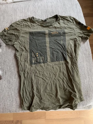 Olivgrön t-shirt Jack & Jones Core - Olivgrön t-shirt från Jack & Jones Core med tryck i svart och gult framtill. Klassisk rund hals och korta ärmar. Skön passform och tillverkad i mjuk bomull. Snygg grafisk design som ger en cool streetkänsla.