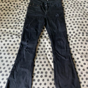 Svarta bootcut jeans med slitningar - Svarta bootcut jeans från Gina tricot i storlek 38. Jeansen har snygga slitningar på benen och klassisk femficksdesign. De är tillverkade i ett mjukt jeansmaterial och har en riktigt skön stretchig passform med utsvängda ben.