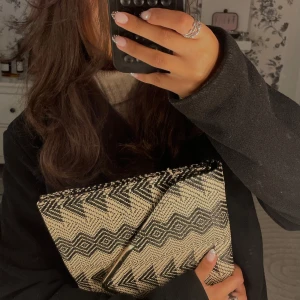 Kuvertväska/datorfodral  - En snygg kuvertväska i svart och beige med grafiskt zigzag-mönster. Kan även fungera som ett datorfodral men var för liten för min dator. Väskan har ett stilrent V-format metallspänne framtill och är tillverkad i ett vävt material som känns både trendigt och unikt! (Aldrig använd) ❤️