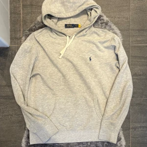 Ralph Lauren Hoodie Grå - Klassisk grå hoodie från Ralph Lauren. Bekväm och stilren modell som fungerar lika bra till vardags som till en mer avslappnad streetwear-look. Ett mångsidigt basplagg i garderoben.