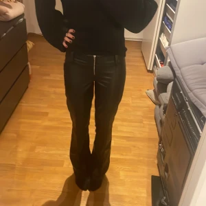 Svarta bootcut byxor i skinnimitation - Säljer ett par svarta byxor i skinnimitation med bootcut-snitt och med låg midja. Helt nya, har bara provat dom nån få gång