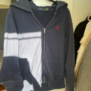 Mörkblå hoodie från Polo Ralph Lauren XS - Mörkblå hoodie från Polo Ralph Lauren i bomull med dragkedja, huva och kängurufickor. Klassisk röd logga broderad på bröstet. Perfekt för chill dagar och enkel att matcha med jeans eller mjukisbyxor. Några defekter därav priset💕
