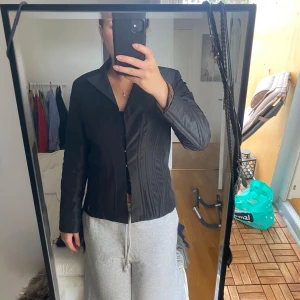 Svart kavaj med markerad midja - Säljer en svart kavaj med klassisk krage och markerad midja. Jackan har lång ärm och knäppning framtill. Snygg och stilren modell som passar perfekt till många olika outfits. Materialet känns slätt och har en lätt glans.