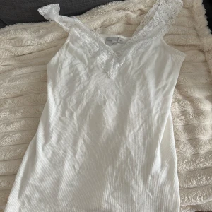 Vit ribbad linnetopp med spets - Supersöt vit ribbad linnetopp från mywear woman med breda axelband i spets och v-ringning framtill. Perfekt att styla med jeans eller kjol för en fräsch look. Mjuk och stretchig bomullskänsla som sitter skönt på kroppen.