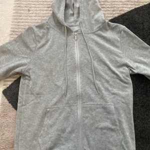 Grå hoodie - En stilren grå hoodie med dragkedja framtill, huva med snörning och två stora fickor. Perfekt för chill dagar eller när du vill ha en enkel och bekväm look. Långärmad och i mjukt bomullsmaterial.