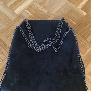 Svart mocka axelväska med kedja - Snygg svart axelväska i mocka med coola silverfärgade kedjor, kommer inte till användning bra för skolan