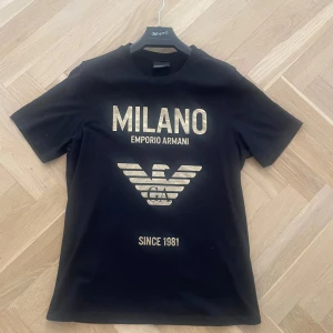 Svart Emporio Armani t-shirt med guldtryck - Svart t-shirt från Emporio Armani. Köptes för 1999kr , pris kan diskuteras vid snabb affär. Finns qr kod