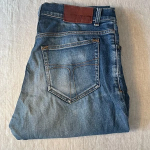Blå jeans från tiger of Sweden  - Snygga blå jeans från T/J i modellen Evolve. Klassisk femficksdesign med ljus tvätt och kontrastsömmar. Skinnpatch bak i midjan. Perfekta för dig som gillar en tidlös jeanslook.