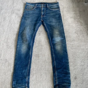 Nudie Jeans - Säljer ett par blå skinny jeans från Nudie Jeans med snygga slitningar och klassiska orange sömmar på bakfickorna. Jeansen har fem fickor, normal midja och är tillverkade i mjukt bomullsjeans. Perfekta för dig som gillar en smal passform och stilren look. Längd 32 och midjan 29! 